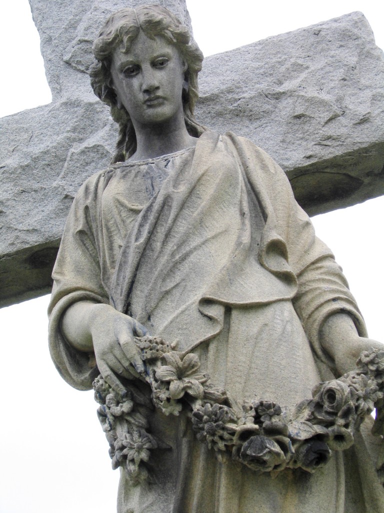 a stone angel with a garland of flowers in front of a cross