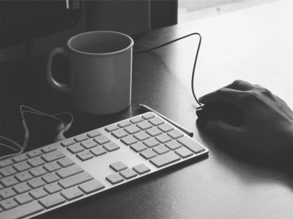 Computer keyboard, hand on mouse, and a coffee mug.